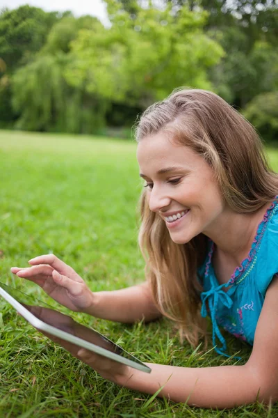 Młoda kobieta uśmiechający się przy użyciu swojego komputera typu tablet leżąc w p — Zdjęcie stockowe