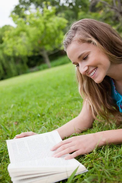 Jovem mulher sorrindo lendo um livro enquanto estava deitado em um parque — Fotografia de Stock