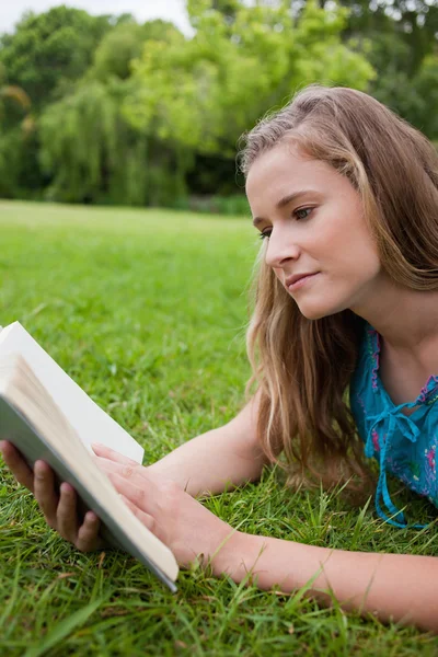 Ciddi genç kadın çim üzerinde yalan sırasında bir kitap okuma — Stok fotoğraf