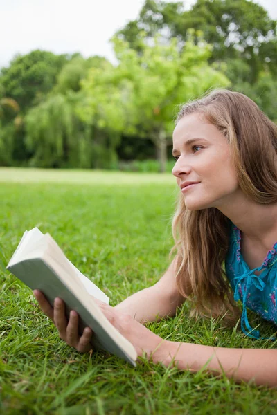 Promyšlené mladá žena držící knihu při pohledu odtud — Stock fotografie