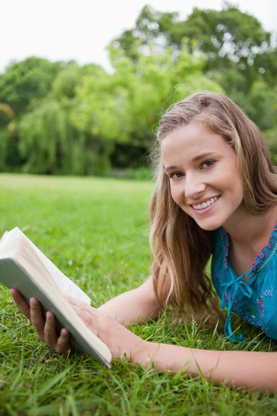 Sorrindo adolescente segurando um livro em um parque enquanto olha — Fotografia de Stock