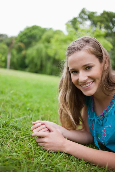 年轻微笑着女人躺在草地上，在一个公共花园 — 图库照片