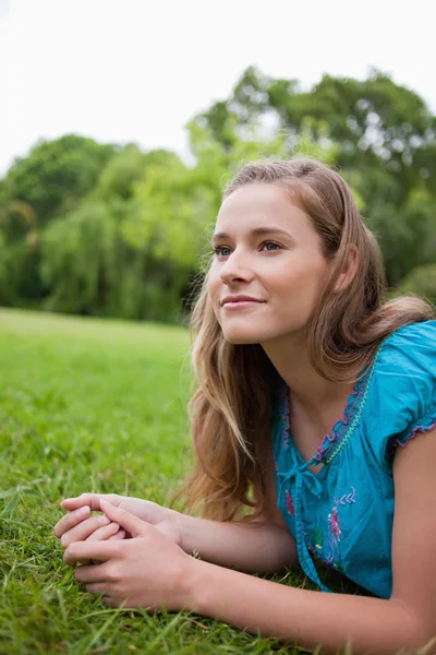 Nachdenkliches junges Mädchen schaut weg, während es im Gras liegt — Stockfoto