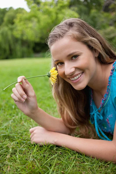 Joven chica sonriente oliendo una flor amarilla mientras está acostado en el g — Foto de Stock