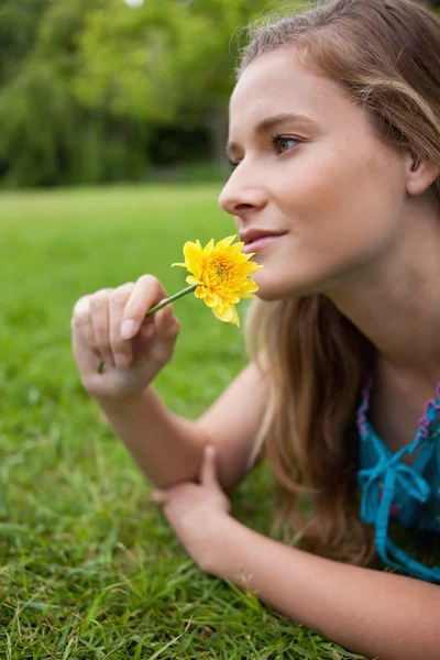 Νεαρή κοπέλα, που βρίσκεται στο γρασίδι, ενώ μυρίζοντας ένα λουλούδι — Φωτογραφία Αρχείου
