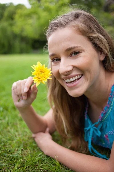 Adolescente sorrindo segurando uma flor amarela enquanto estava deitado no gras — Fotografia de Stock