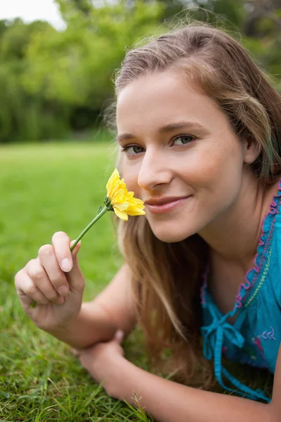年轻微笑女孩同时嗅到的一朵花和我躺在一个公园 — 图库照片