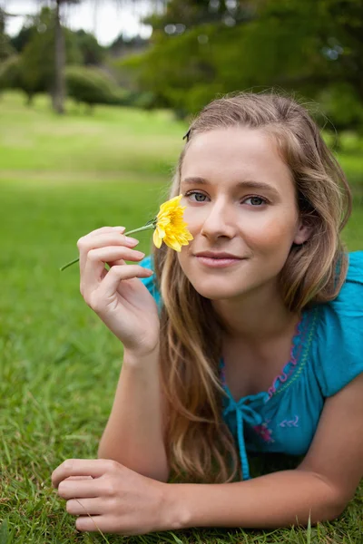 Jovem menina relaxada segurando uma flor amarela enquanto deitado em um parque — Fotografia de Stock