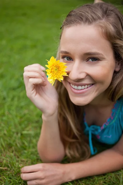 Mujer joven sonriente mostrando una flor amarilla mientras está acostada en la g — Foto de Stock