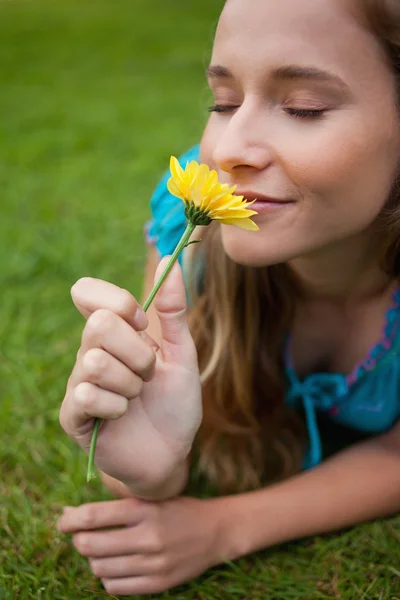Jovem menina relaxada cheirando uma flor enquanto deitado na grama — Fotografia de Stock