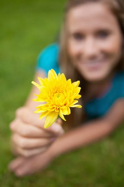 Žlutý květ, drží mladou dívku ležící na trávě — Stock fotografie