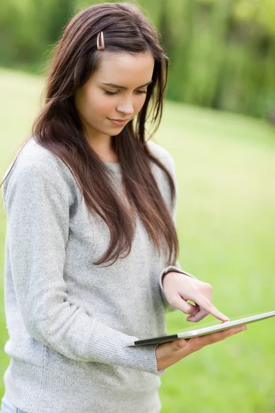 Серйозна молода жінка стоїть під час використання свого планшетного комп'ютера — стокове фото