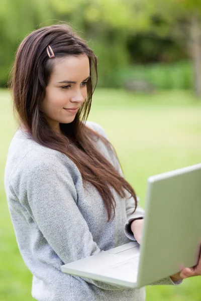 Junge entspannte Frau hält ihren Laptop während sie in einem Park steht — Stockfoto