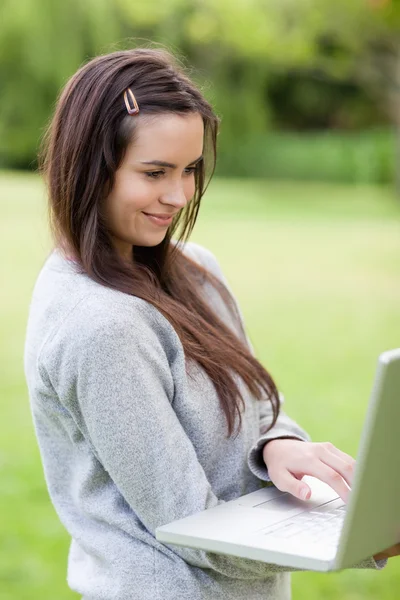 Smiling young woman holding her laptop while standing in a publi — Stock Photo, Image