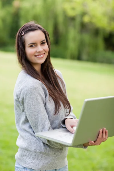 Молодая улыбающаяся женщина держит свой ноутбук, стоя прямо в — стоковое фото