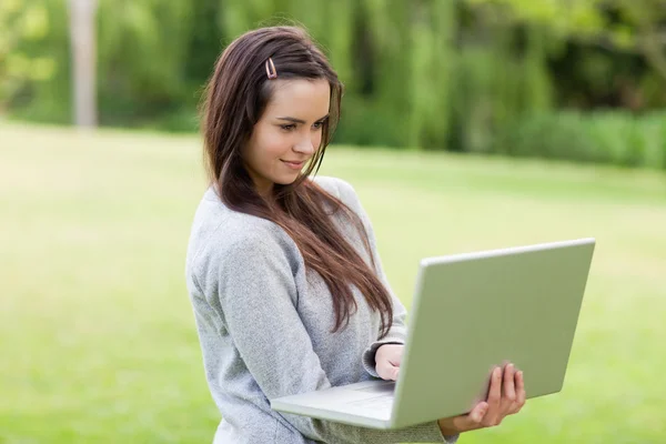 Serious young woman standing upright in a park while holding her — Stock Photo, Image