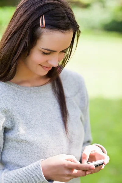 Entspanntes junges Mädchen, das einen Text mit ihrem Handy sendet, während sie — Stockfoto