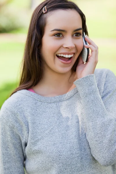 Удивлена, что молодая женщина разговаривает по телефону, стоя в р — стоковое фото