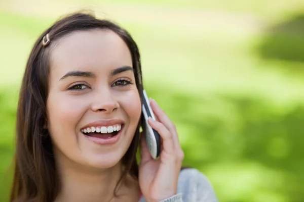 Jonge vrouw met behulp van haar mobiele telefoon in een park terwijl lachen — Stockfoto