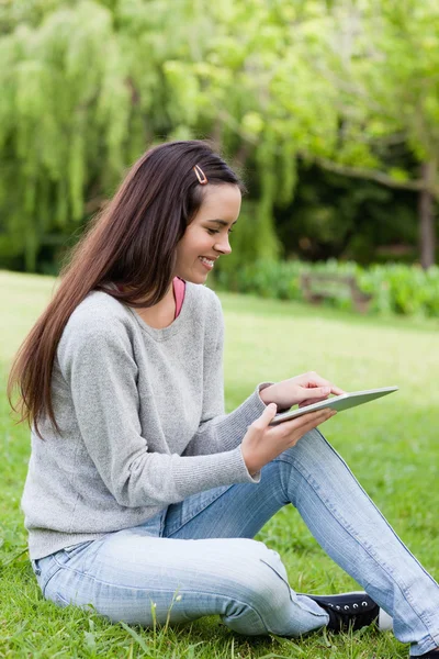 微笑着坐在一个公园的同时使用她的 tablet pc 的年轻女孩 — 图库照片