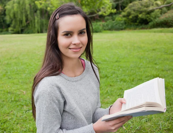 Smiling young girl standing upright in the countryside while rea — Stock Photo, Image