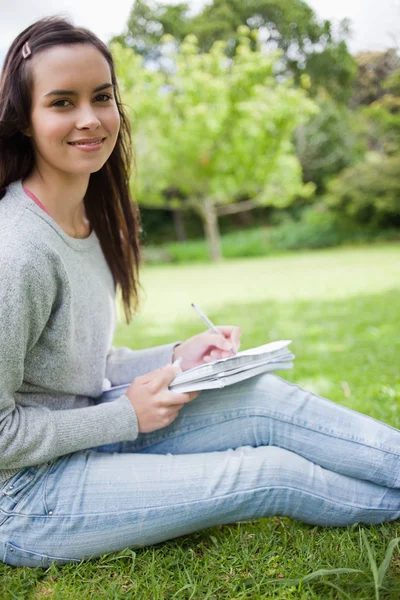 Joven chica sonriente sentada en el campo mientras hace su ho — Foto de Stock