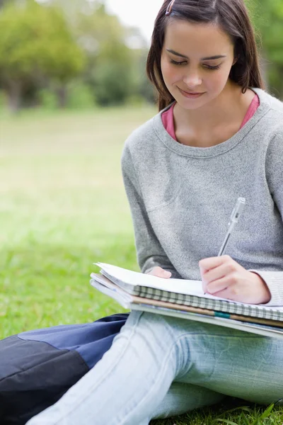 Menina sorrindo jovem escrevendo em seu caderno enquanto sentado em um pa — Fotografia de Stock