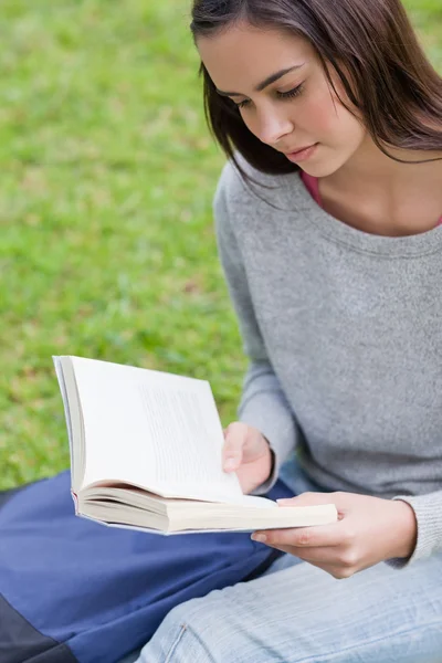 Ernstige jong meisje, zittend op het gras tijdens het lezen van een boek — Stockfoto