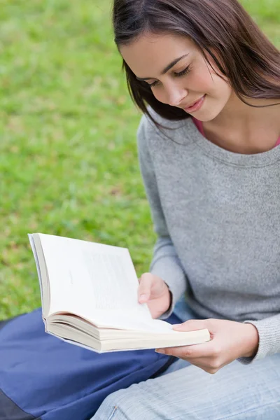 Jonge ontspannen meisje zit in een openbare tuin tijdens het lezen van een bo — Stockfoto