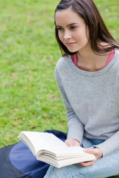 Jovem mulher calma lendo um livro em um parque enquanto olha para — Fotografia de Stock