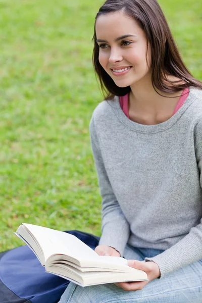 Uśmiechnięta młoda kobieta szuka od trzymając książkę — Zdjęcie stockowe