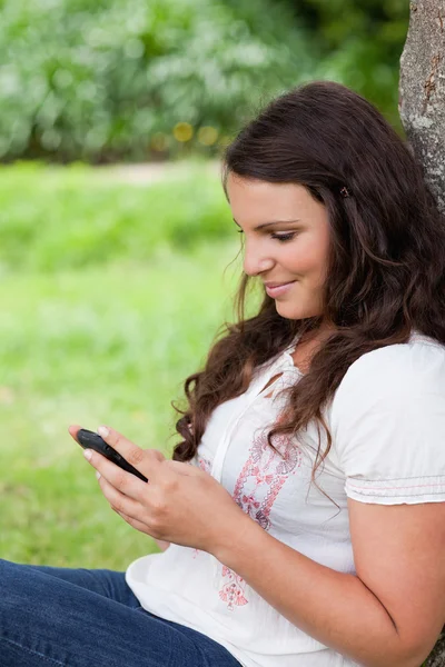 Junge entspannte Frau schreibt einen Text, während sie gegen einen Baum sitzt — Stockfoto