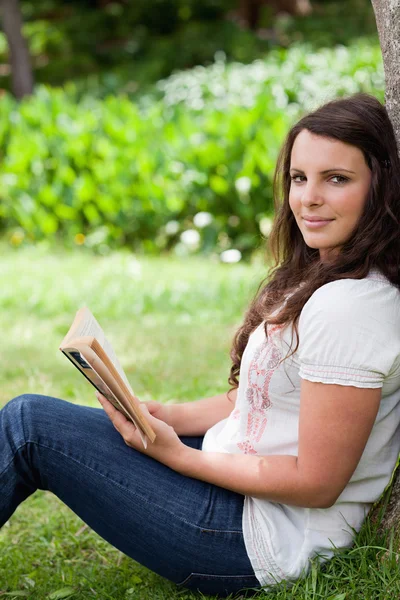 Junge entspannte Frau blickt in die Kamera, während sie ein Buch in der Hand hält — Stockfoto