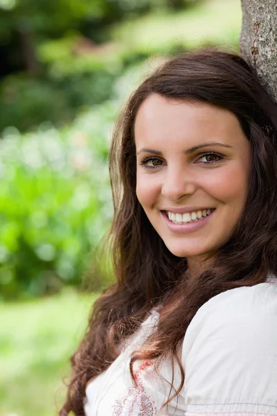 Young woman leaning against a tree while showing a beaming smile — Stock Photo, Image