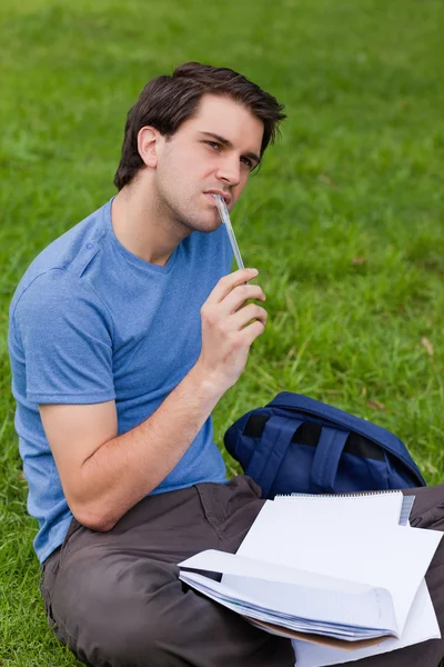 Mladý přemýšlivý muž drží pero, zatímco sedí na trávě — Stock fotografie