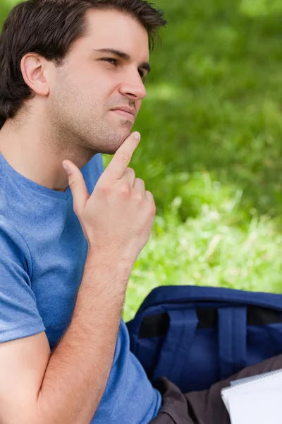 Молодой человек кладет палец на подбородок, сидя в парке — стоковое фото