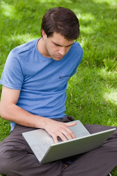 Vážný mladík pracuje na jeho laptopu, zatímco sedí v parku — Stock fotografie