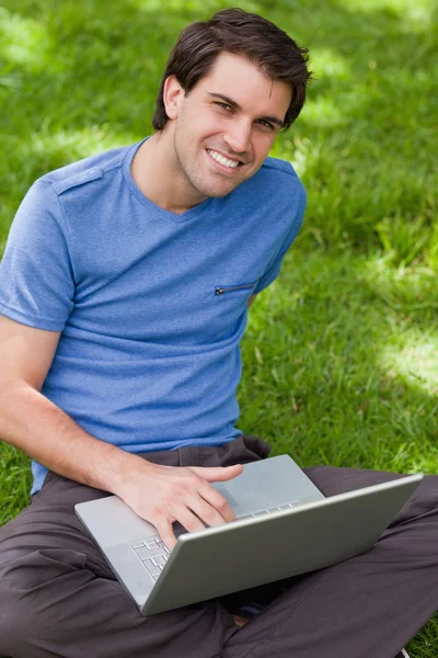 足を組んで坐っている間彼のラップトップを使用して若い笑みを浮かべて男 — ストック写真