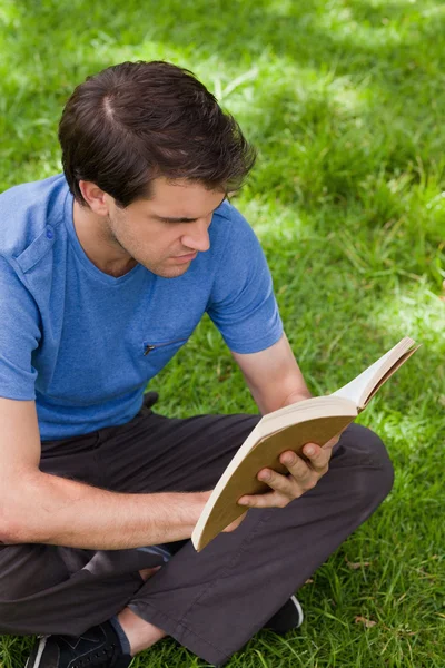 Jovem homem sério sentado de pernas cruzadas enquanto lê um livro — Fotografia de Stock
