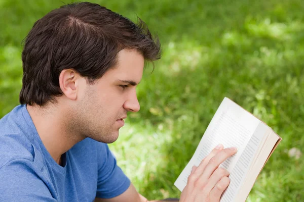 Σοβαρές νεαρός διαβάζοντας ένα βιβλίο, ενώ κάθεται σε ένα πάρκο — Φωτογραφία Αρχείου