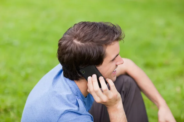 Young smiling man talking on the phone while sitting in a park — Stock Photo, Image