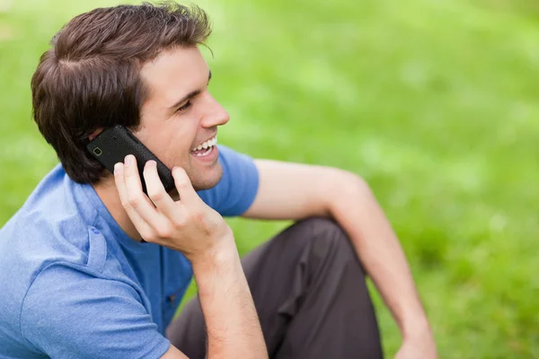 Young man talking on the phone while sitting on the grass — Stock Photo, Image