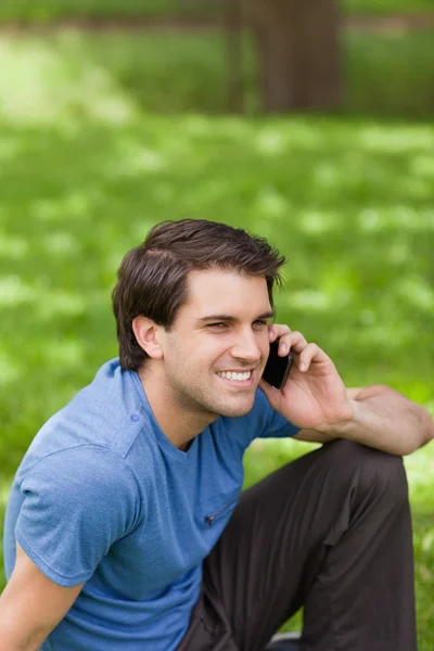 Jovem sorrindo homem chamando com seu celular enquanto sentado em um — Fotografia de Stock