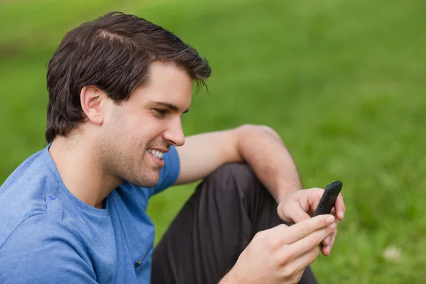 Young man sending a text with his cellphone while sitting on the — Stock Photo, Image