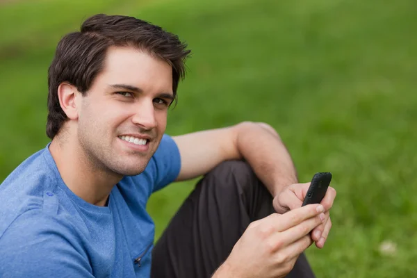Boldog fiatal ember nézi a kamerát egy szöveg küldésekor — Stock Fotó