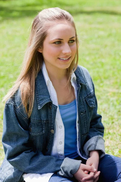 Menina sorrindo jovem sentado na grama com as mãos cruzadas — Fotografia de Stock