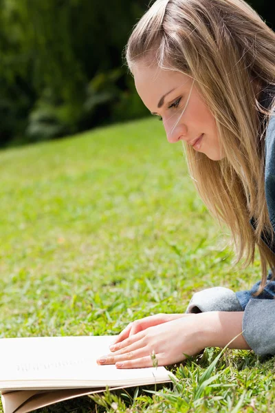 Young blonde girl lying on the grass while reading a book — Stock Photo, Image