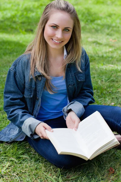 Fiatal lány ül törökülésben, miközben tartja a könyvet, és keres — Stock Fotó