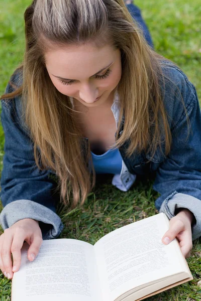 Молода розслаблена дівчина лежить на траві під час читання книги — стокове фото