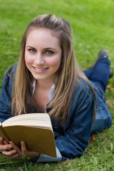 Joven chica feliz acostada en la hierba mientras sostiene un libro y un baño — Foto de Stock
